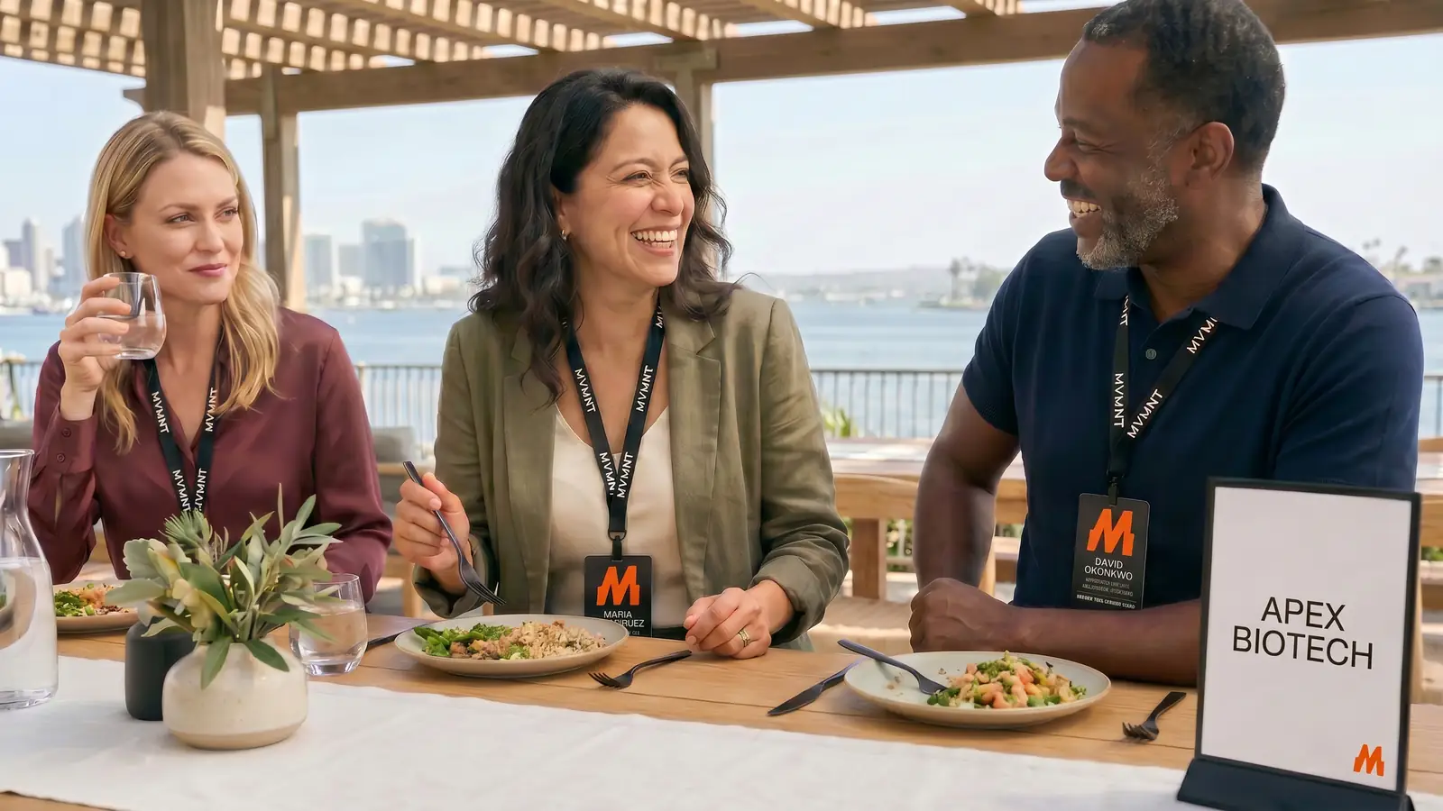 A hosted networking lunch on the Loews terrace, three physicians mid-conversation with a partner-host card on the table.