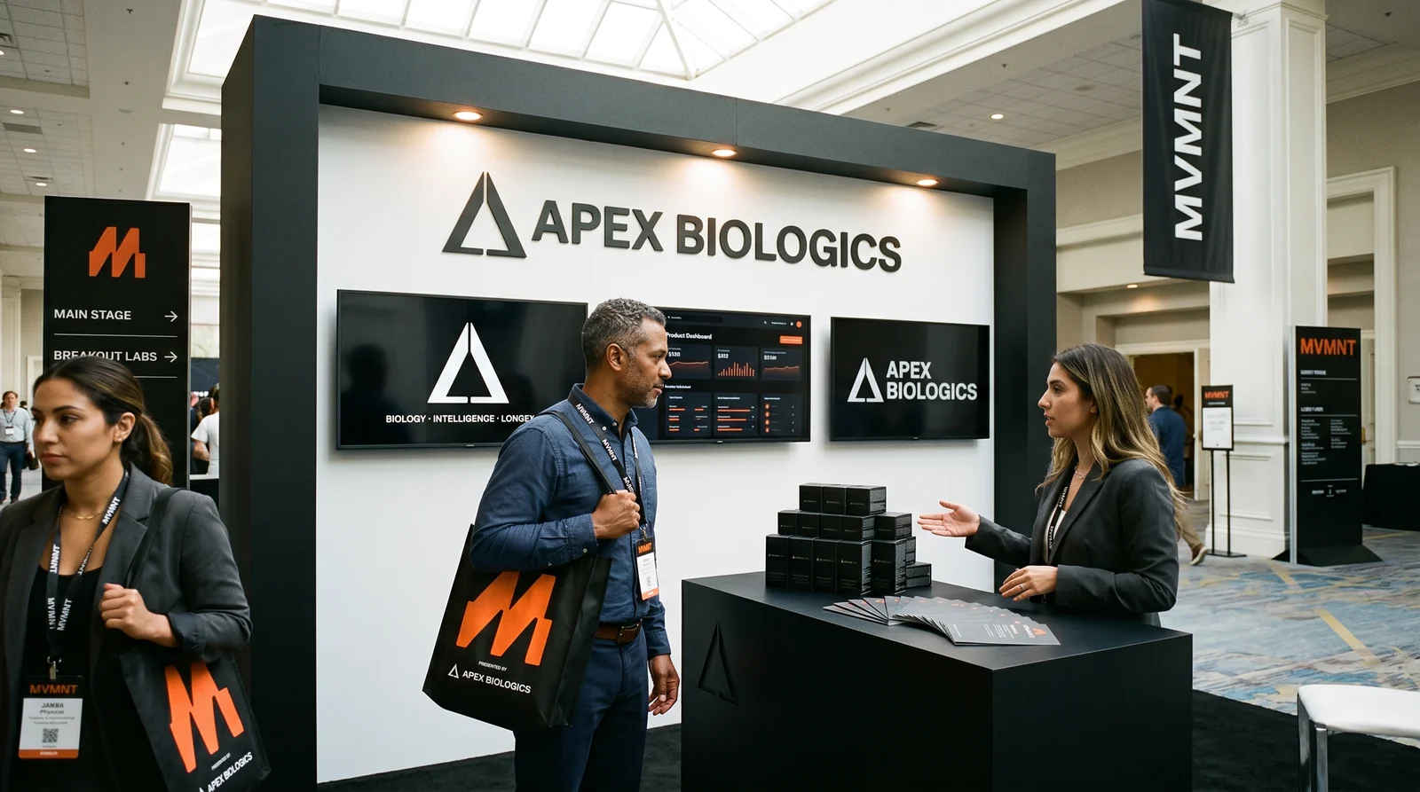 Two physicians engaging at an Apex Biologics exhibit booth; an attendee passes with a partner-branded MVMNT conference bag.