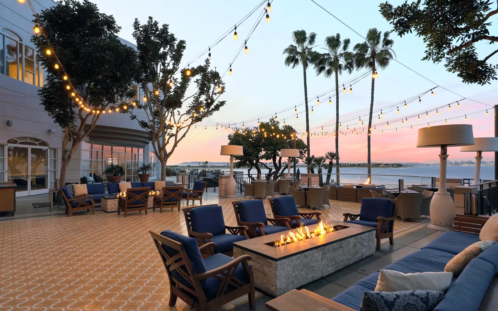 The terrace with string lights and firepit at sunset, bay beyond.
